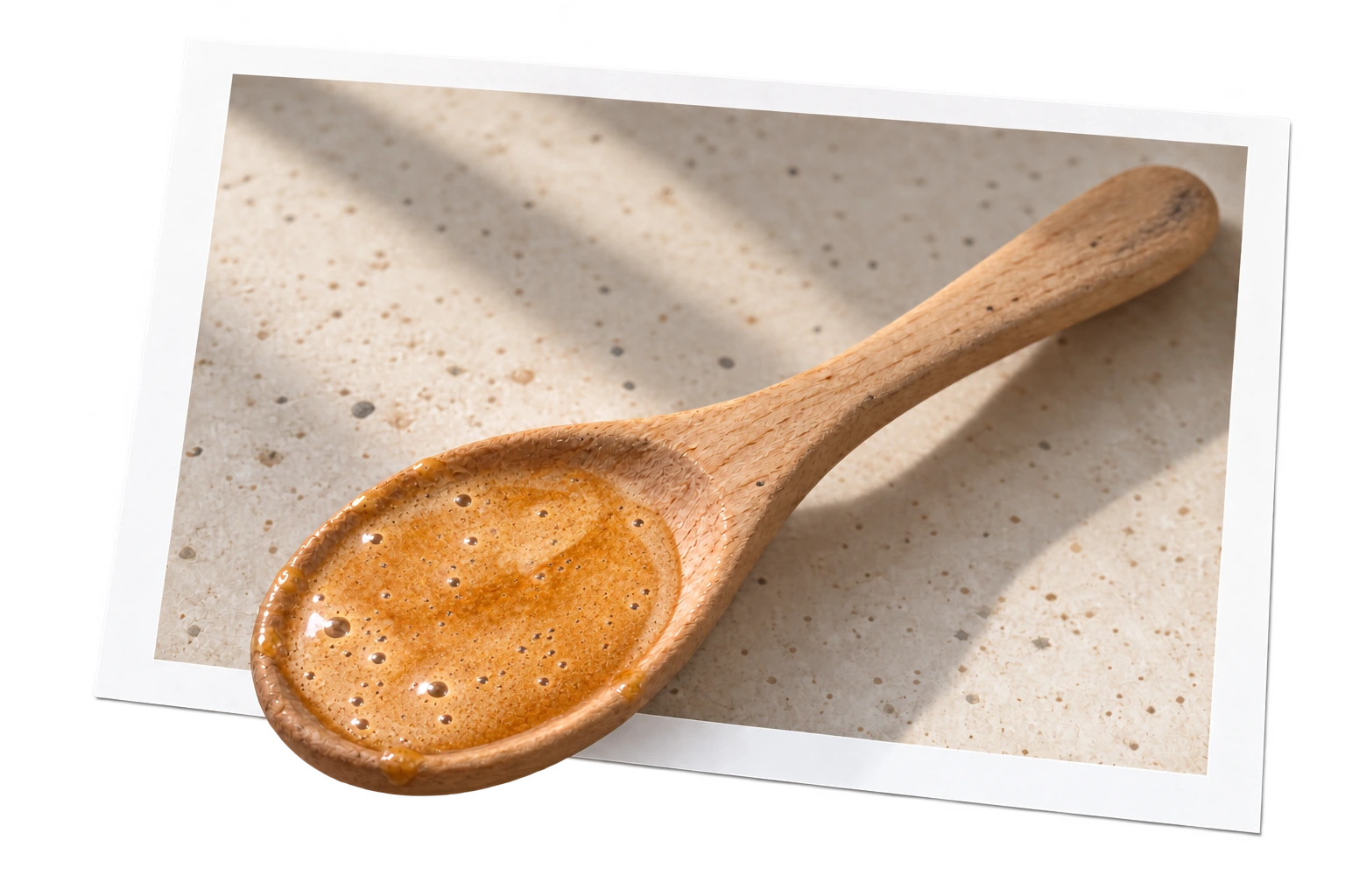 A slender wooden spoon filled with creamy honey blend extending out of a white-bordered photograph